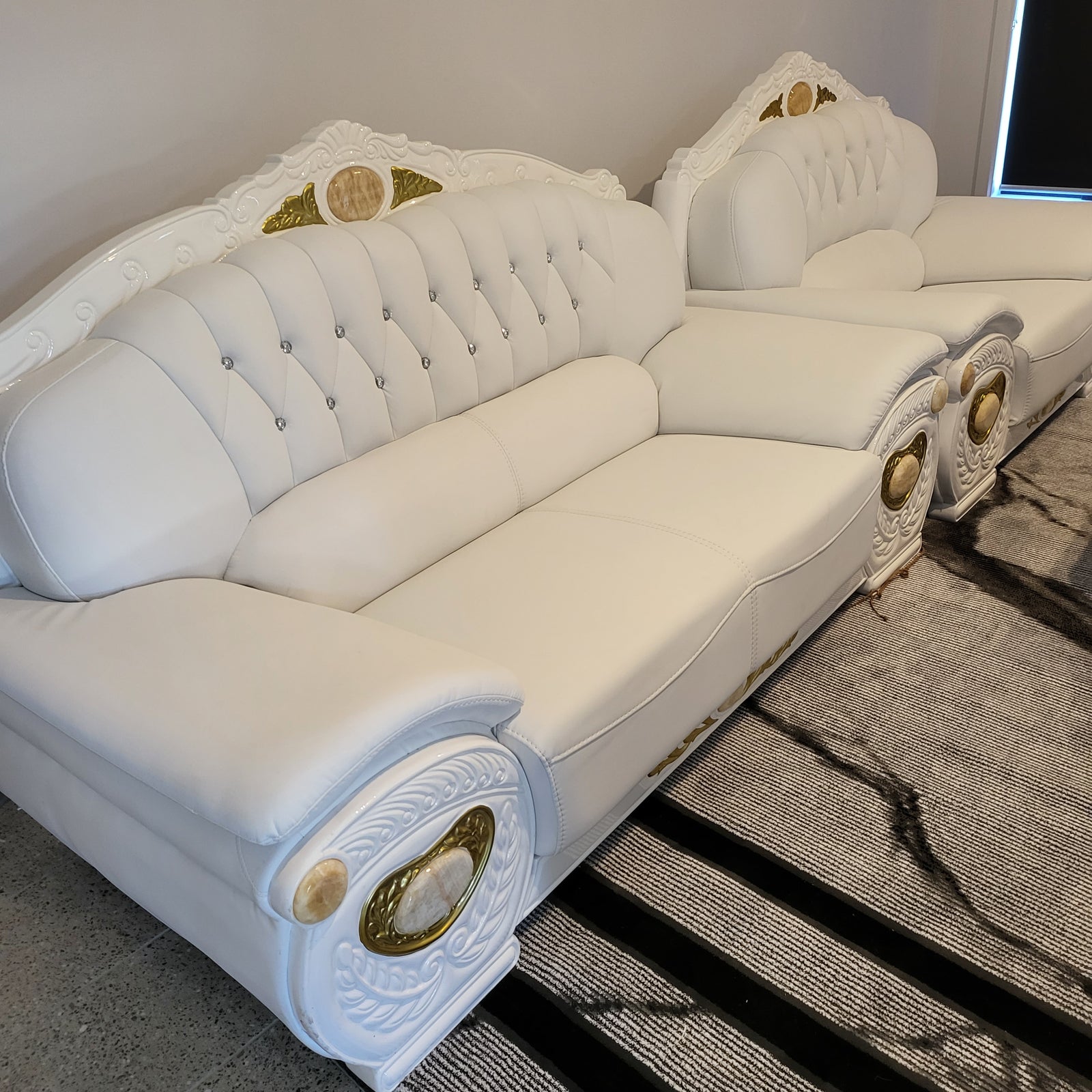 White sofa with decorative buttons and gold accents against a wooden wall.