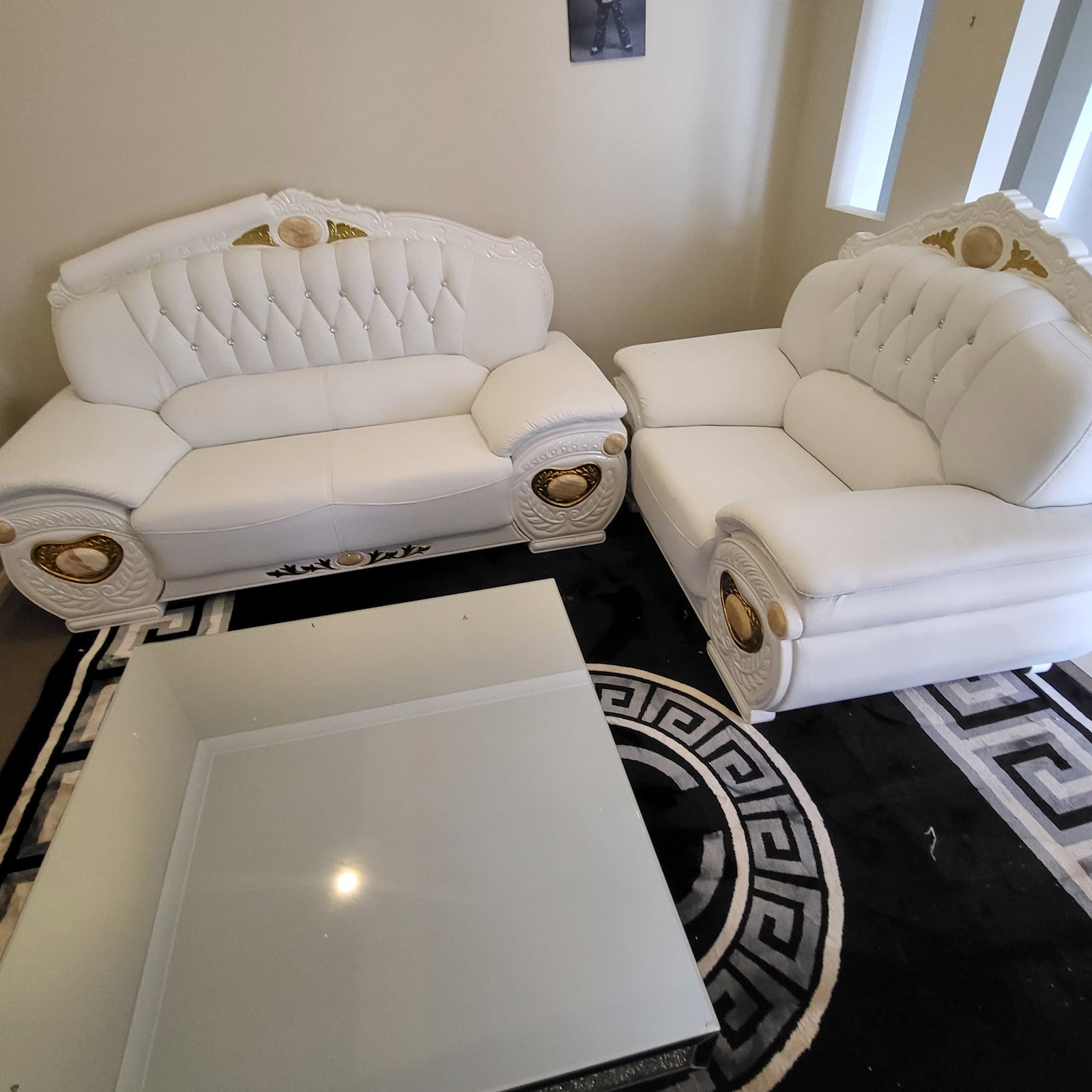 White leather sofa with gold accents in a room with a decorative rug.