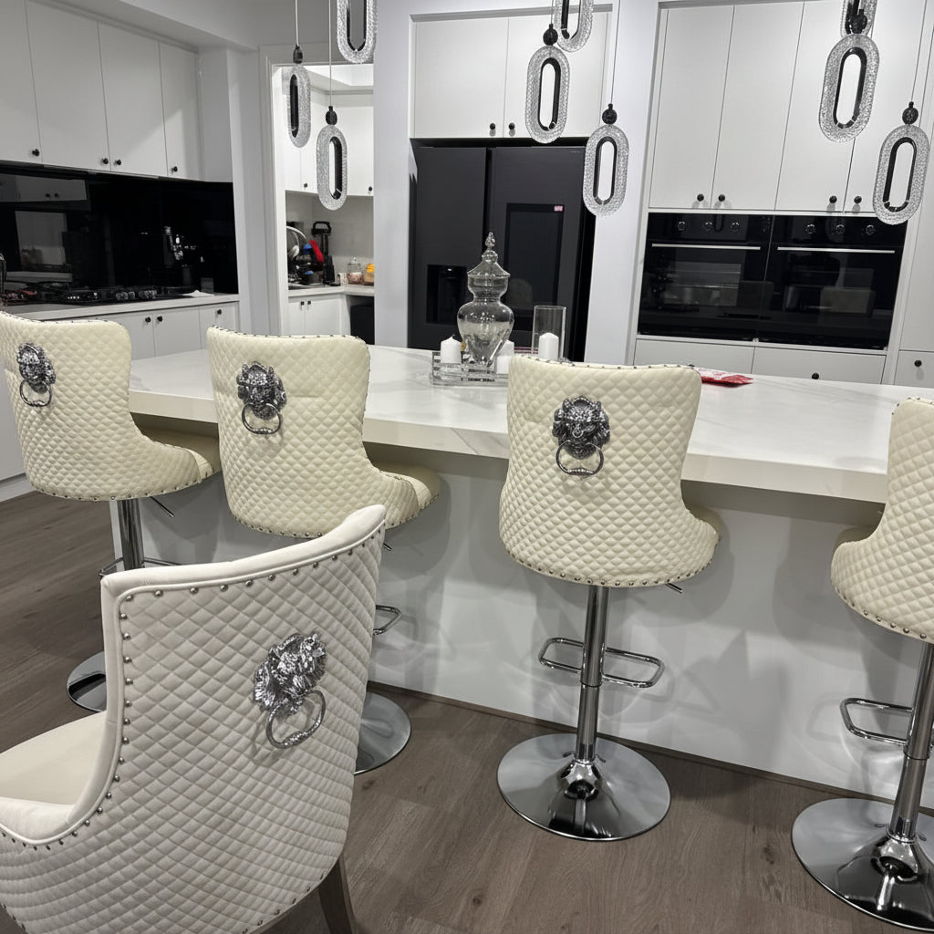 A set of modern bar stools with quilted cream upholstery and silver metal bases, arranged around a white kitchen island in a contemporary kitchen setting.
