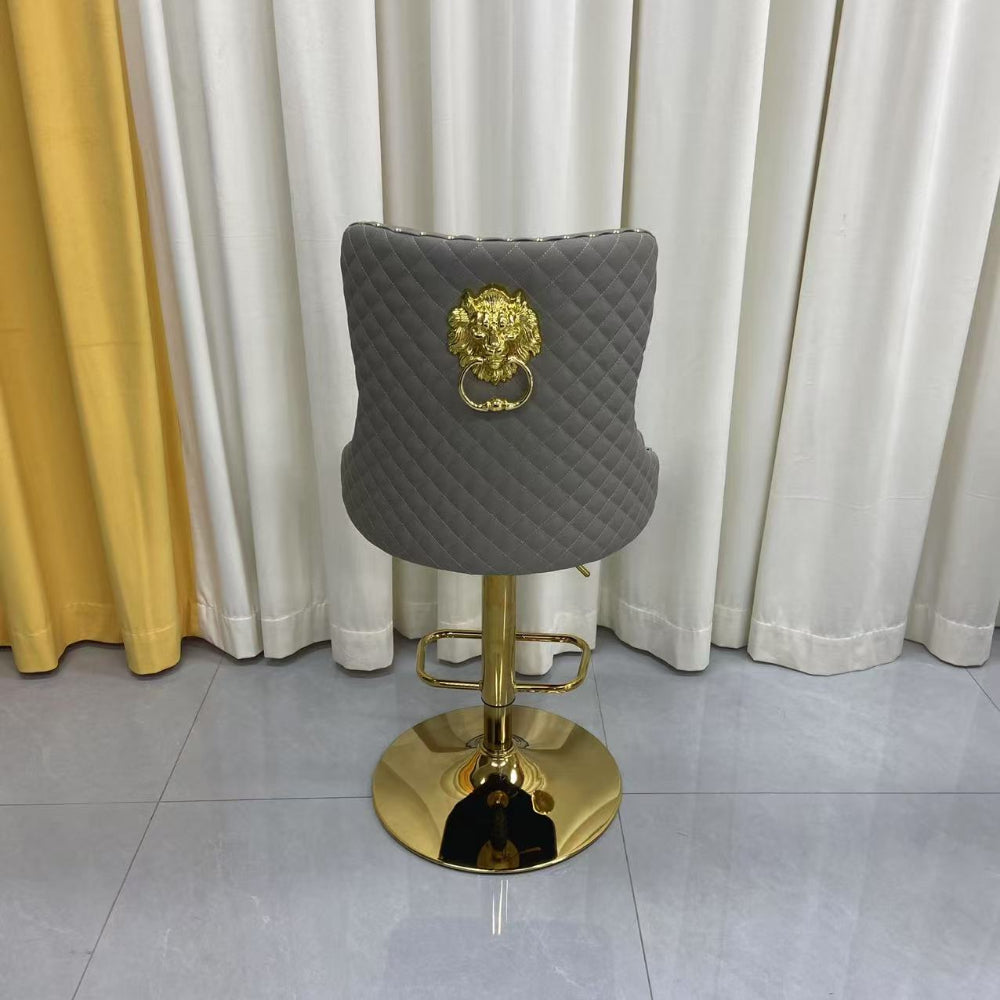 Grey Leather quilted bar stool with gold base and lion emblem against a white curtain background