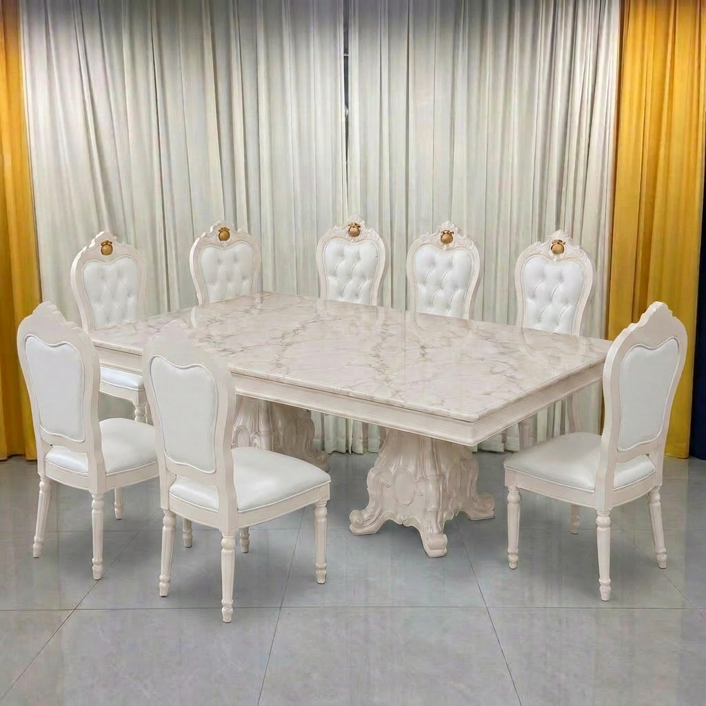 An elegant dining set featuring a rectangular white marble-patterned table with a carved pedestal base, surrounded by six matching white upholstered chairs with tufted backs and gold accent details.