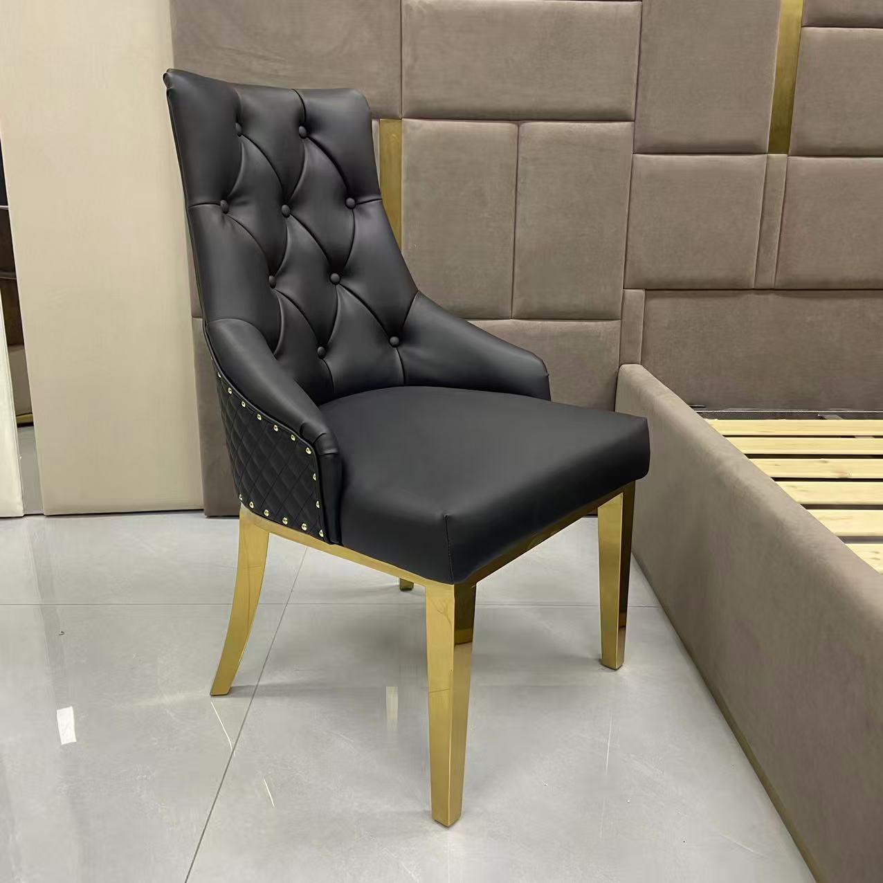Black upholstered chair with gold legs in a room with beige walls and tiled floor.