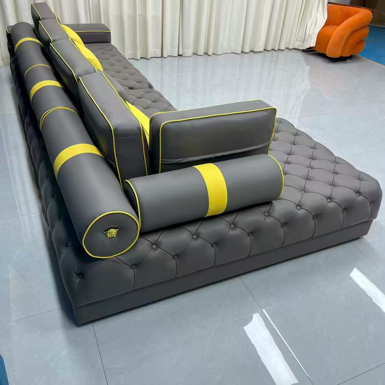 Gray tufted sofa with yellow accents on a reflective floor.