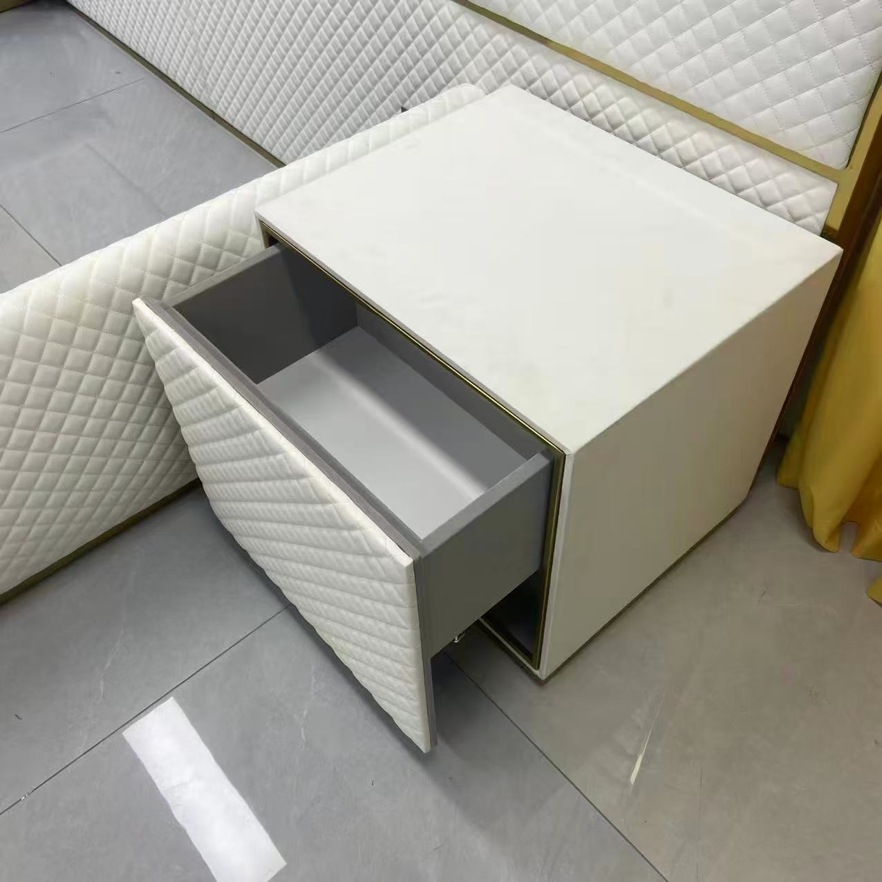 White nightstand with open drawer against a textured wall.