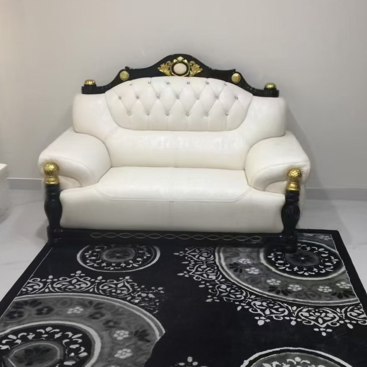 White leather sofa with black and gold accents on a black patterned rug.