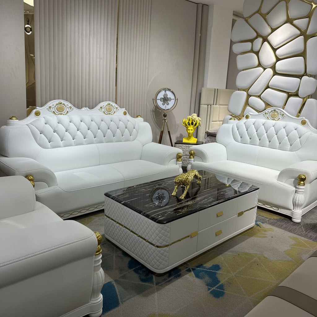 Luxury white leather sofa set with gold accents, featuring a tufted chaise lounge, matching armchair, and a matching coffee table with a black marble top, set in a modern living room.