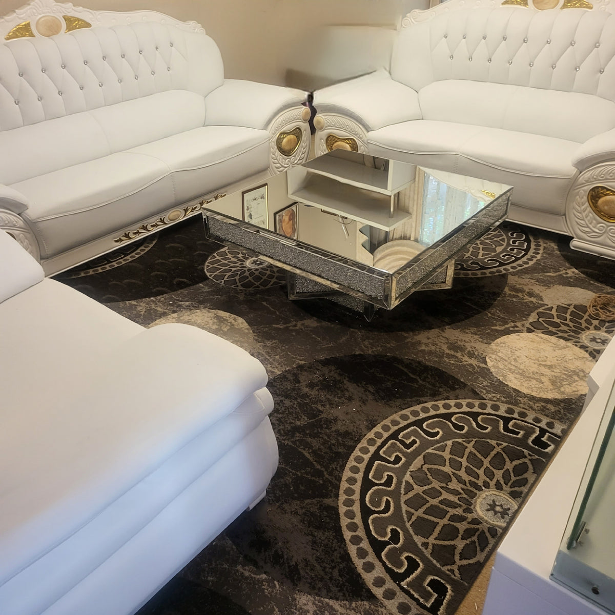White leather sofa set with a reflective coffee table on a patterned rug.