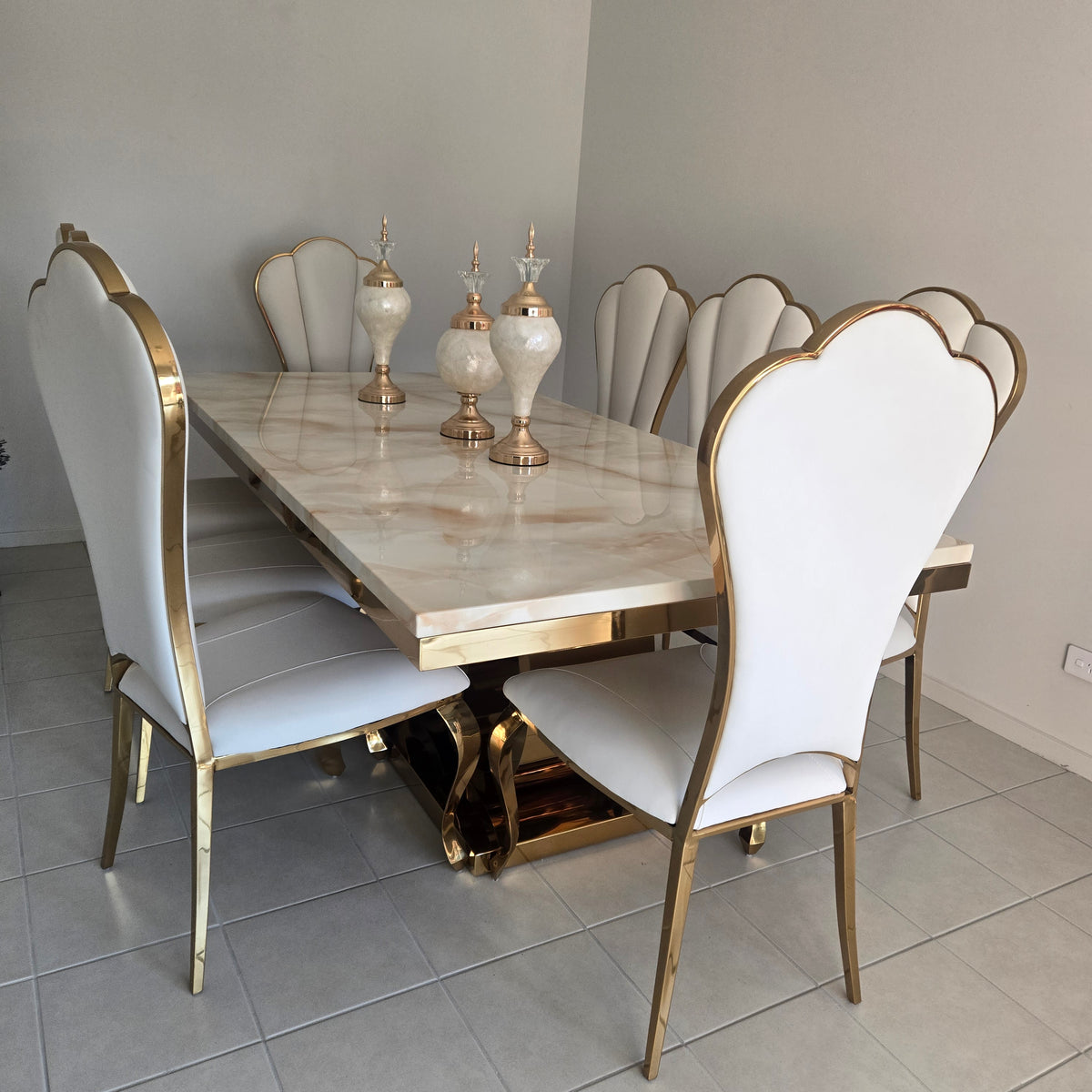 Dining table set with white chairs and gold legs in a room with gray tiled floor.