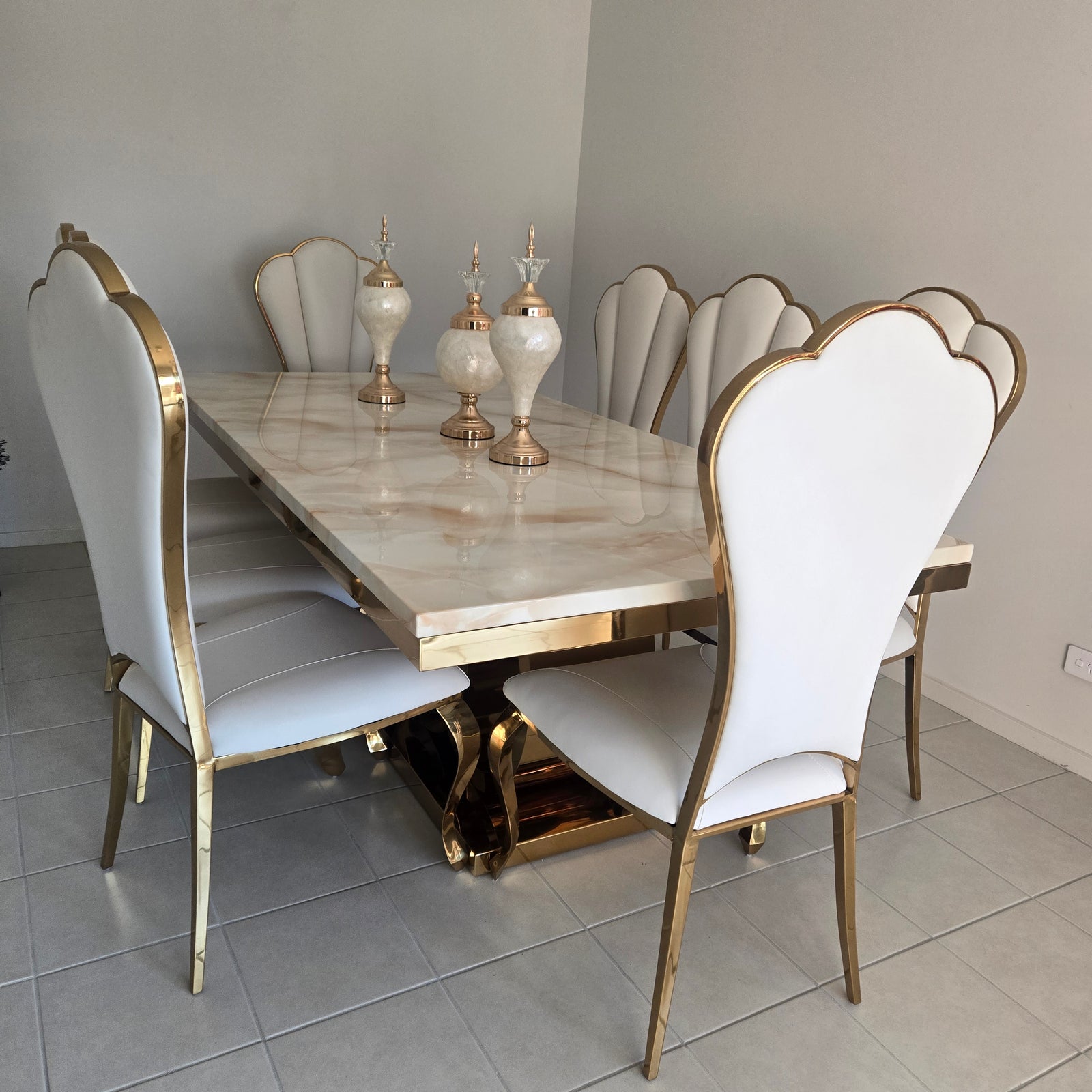Dining table set with white chairs and gold legs in a room with gray tiled floor.