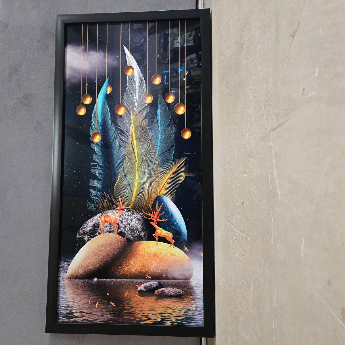 Framed artwork with abstract design of feathers, deer, and stones on a gray wall.