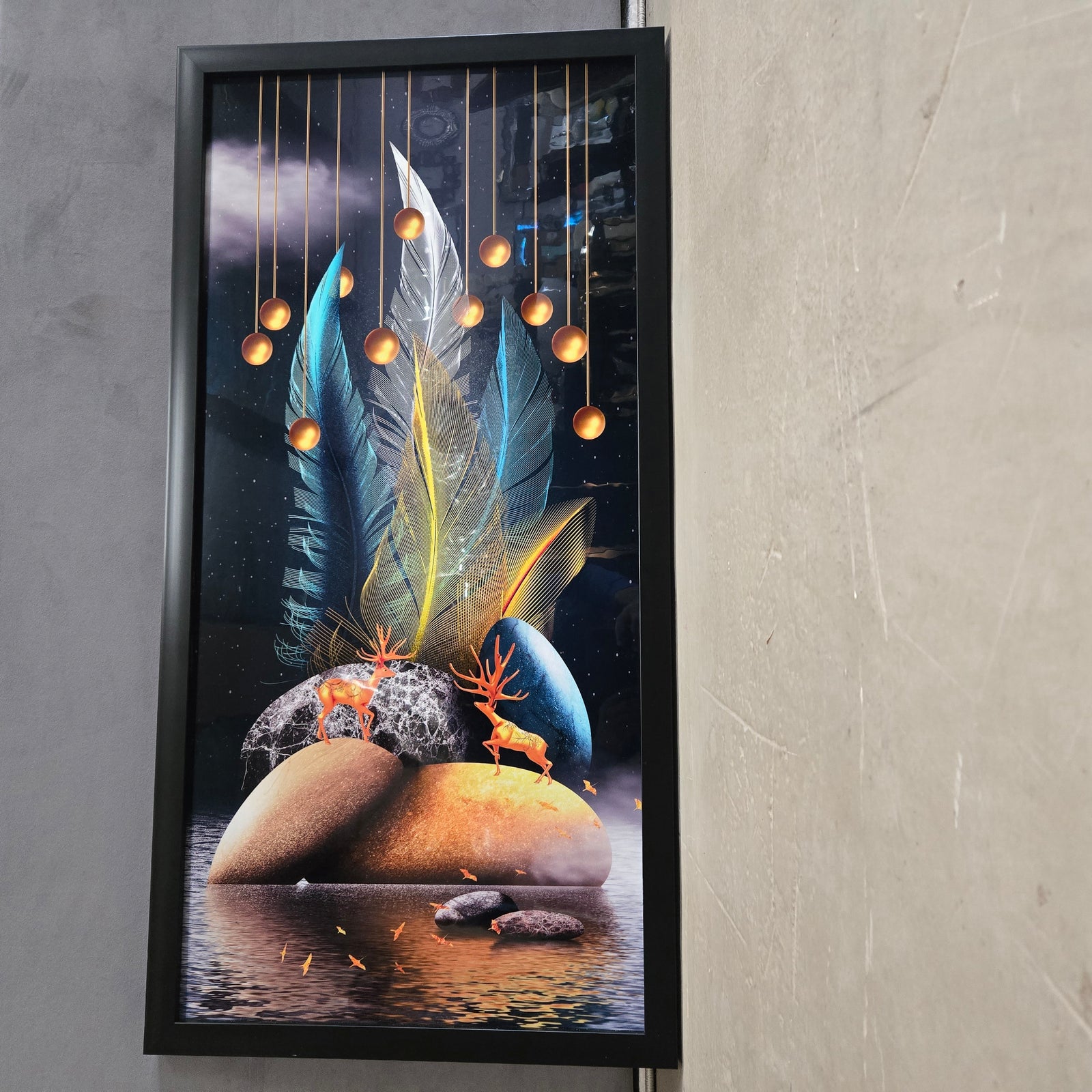 Framed artwork with abstract design of feathers, deer, and stones on a gray wall.