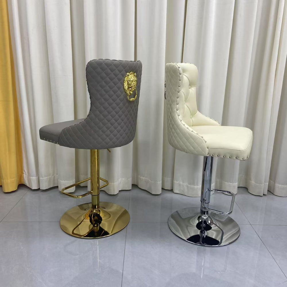 Two bar stools, one gray with gold base and lion emblem, the other white with chrome base, against a white curtain background.