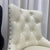 Cream-colored bar stool with a tufted backrest against white curtains.