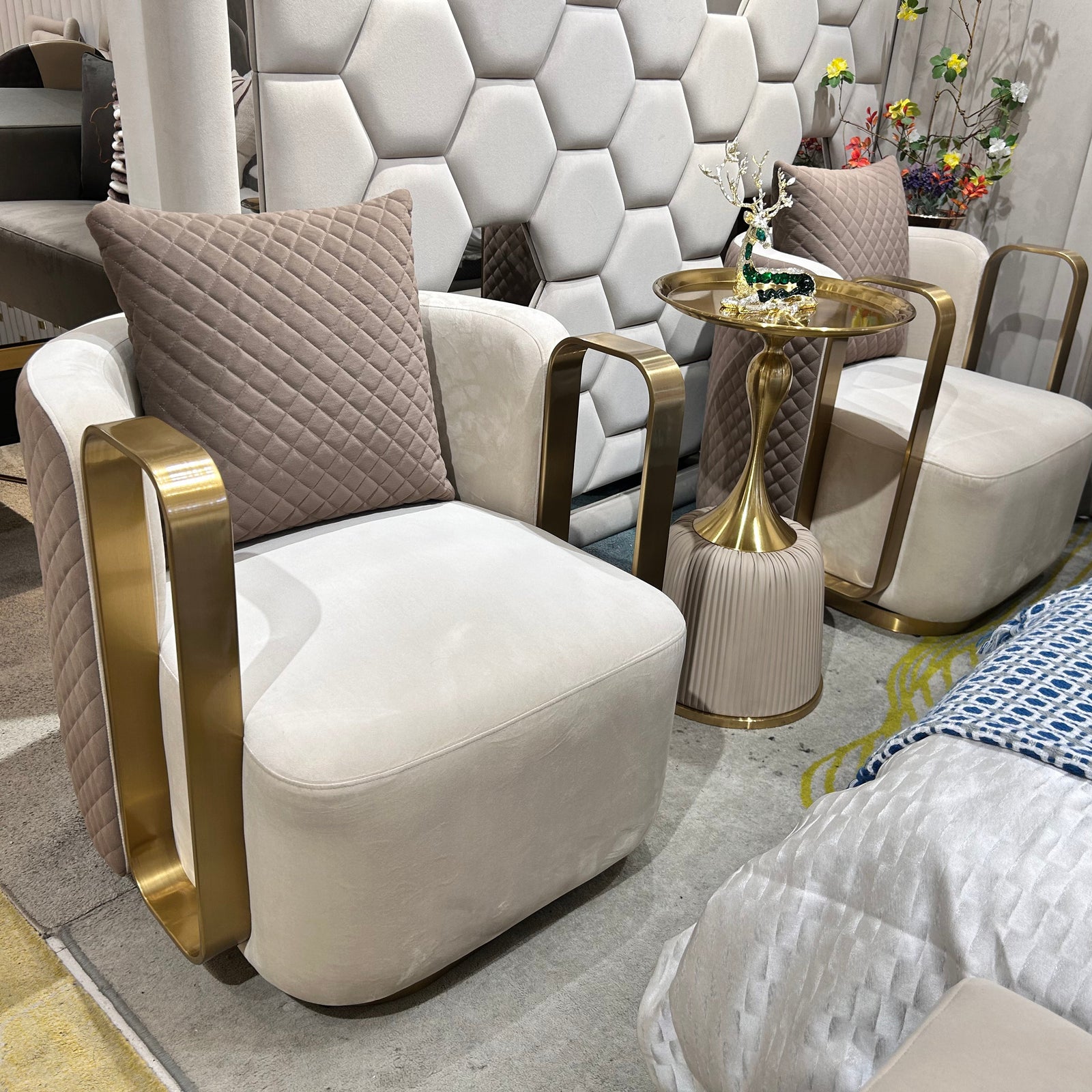Two cream accent chairs with gold-tone arm detailing and quilted outer panels, styled beside a round pedestal table.