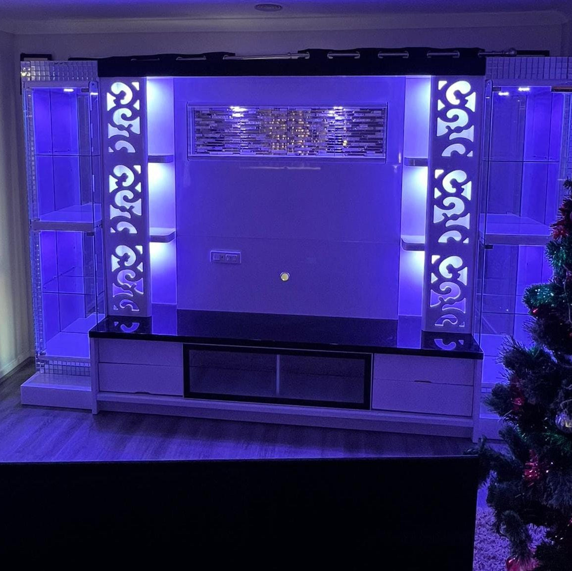 Modern entertainment center with decorative elements and a Christmas tree in a living room.
