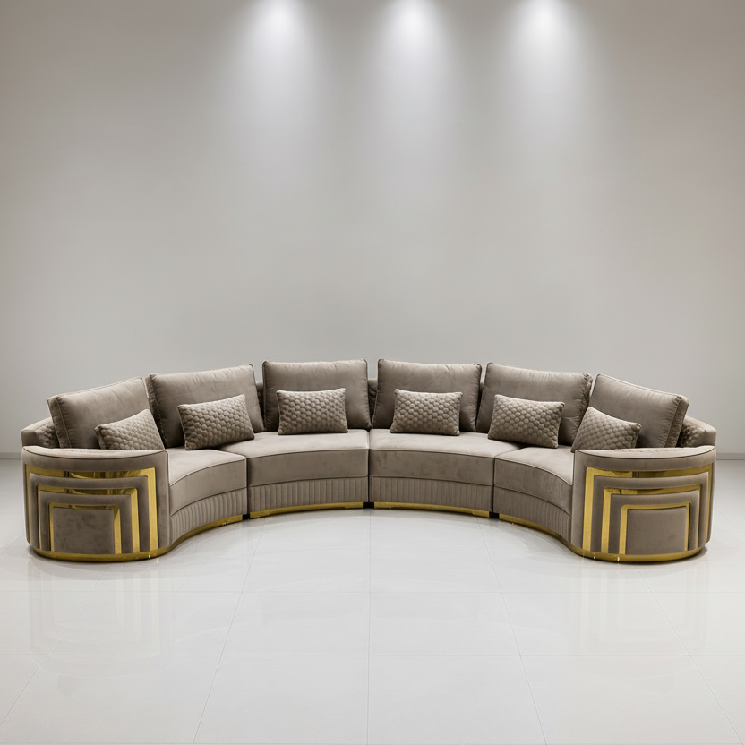 A curved modular upholstered sofa set in a bright, minimalist showroom. The set includes a U-shaped sectional sofa and a matching armchair, both upholstered in a textured taupe fabric with prominent gold geometric frame accents on the outer sides.