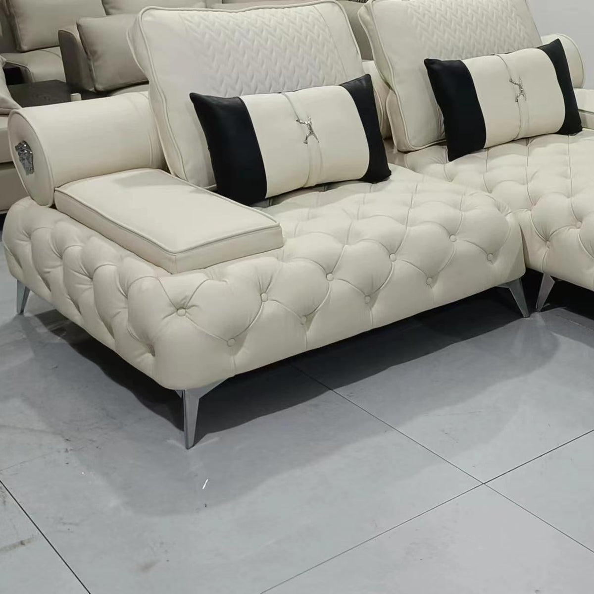 Beige sectional sofa with black and white pillows on a tiled floor.