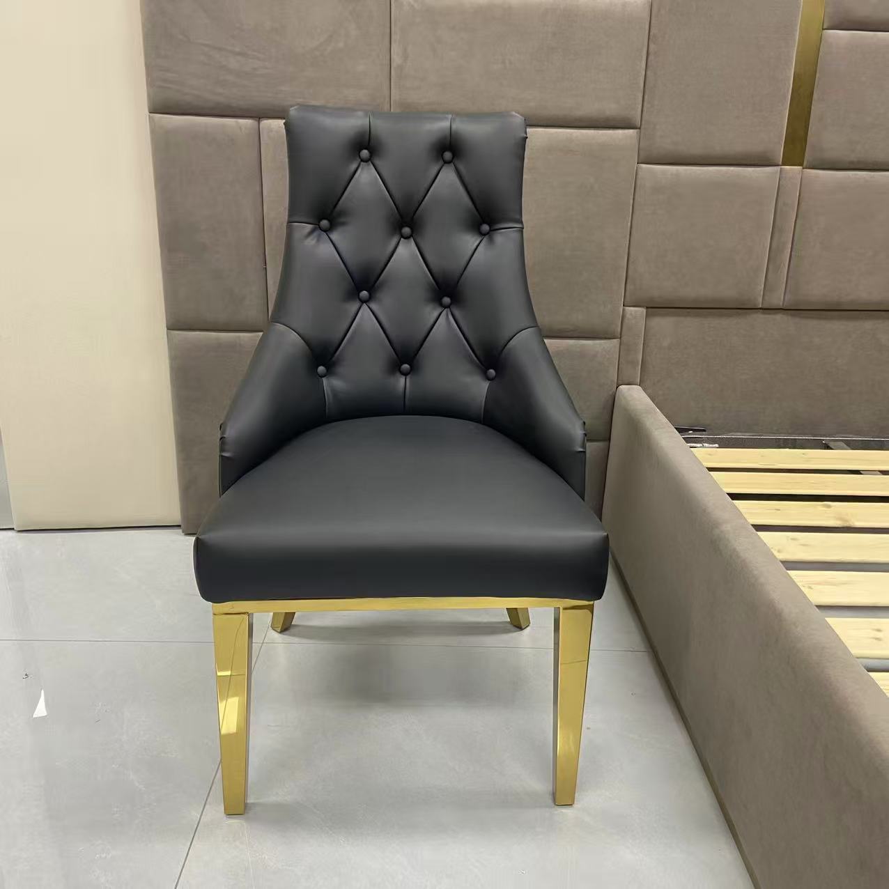 Black upholstered chair with gold legs in front of a beige wall.