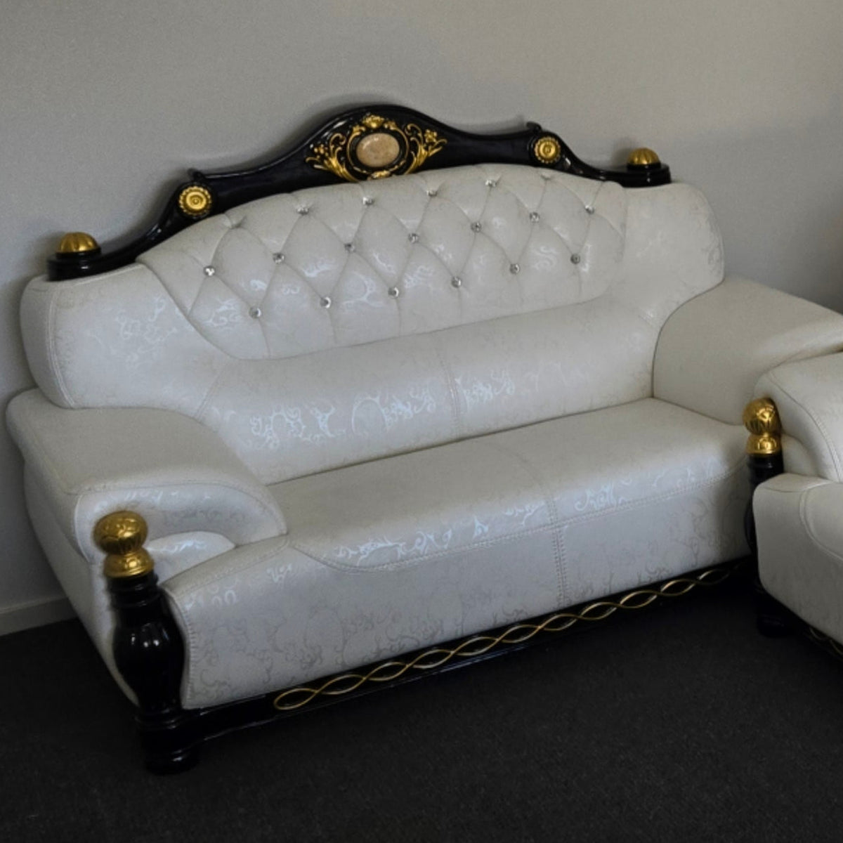 White leather sofa with decorative black and gold accents against a plain wall.
