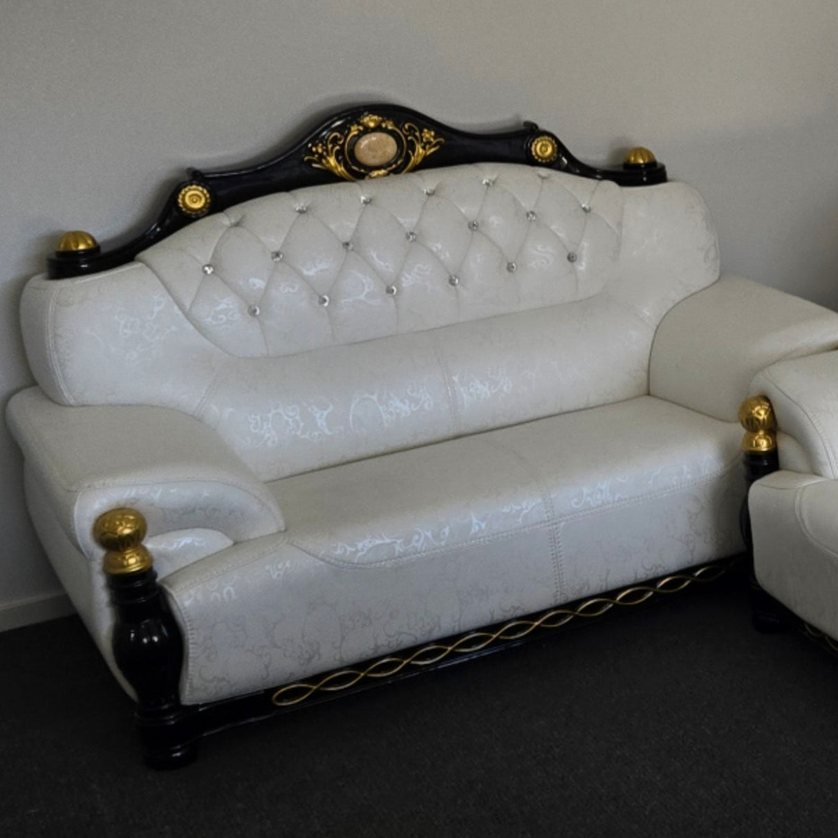 White leather sofa with decorative black and gold accents against a plain wall.