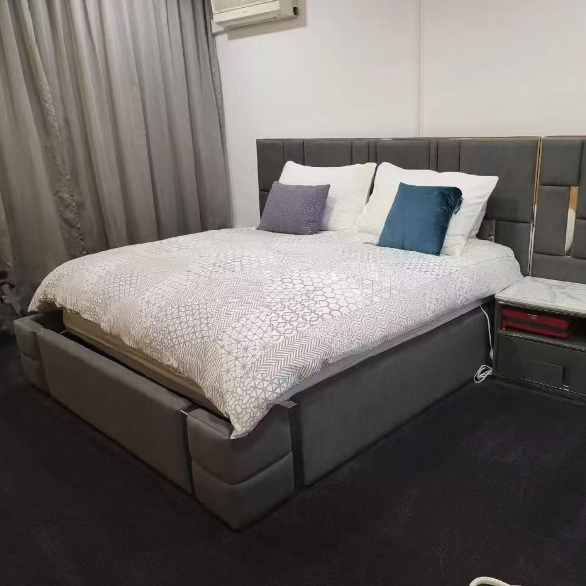 Gray upholstered bed with white bedding and blue pillows in a bedroom setting.