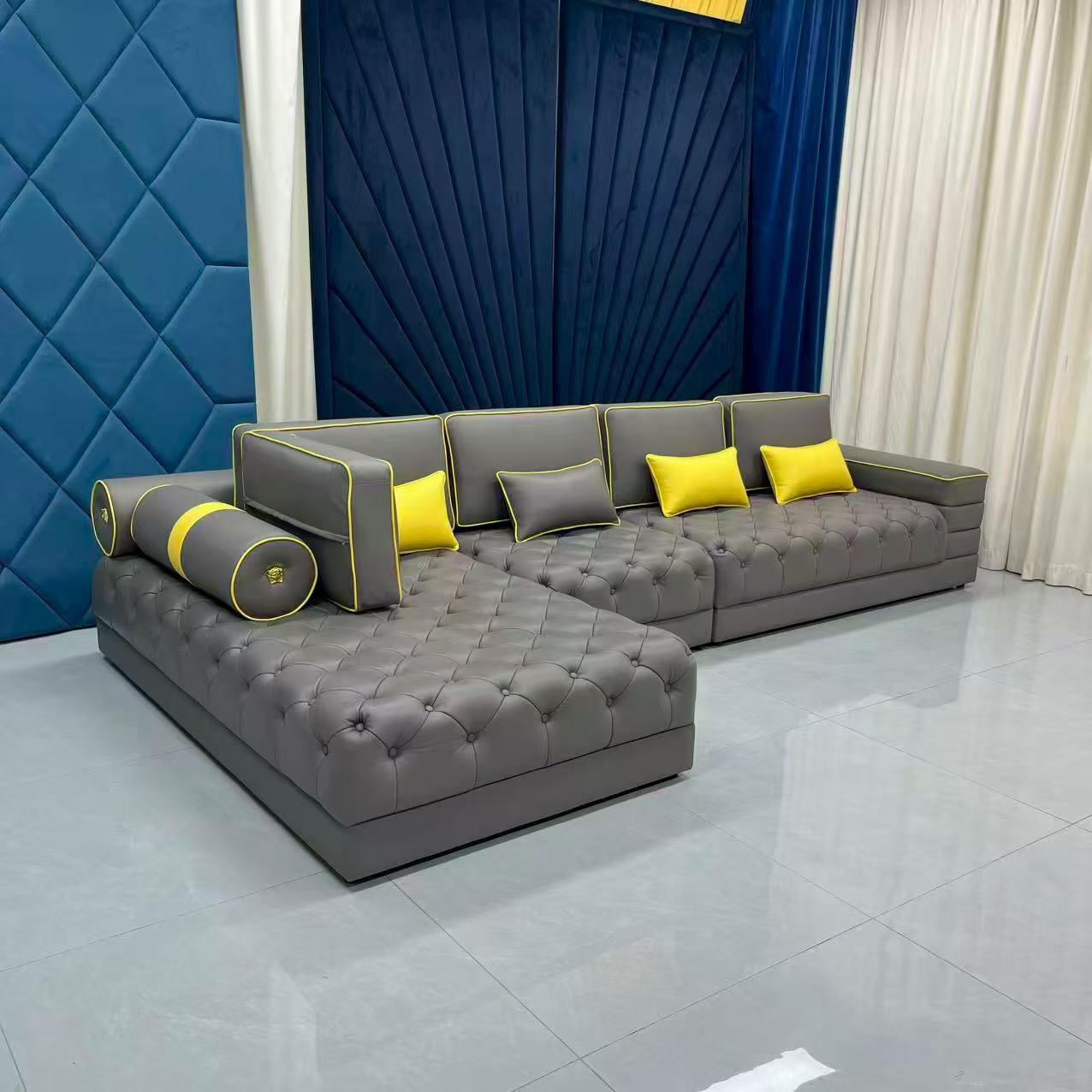 Gray sectional sofa with yellow cushions against a blue wall and white curtains.