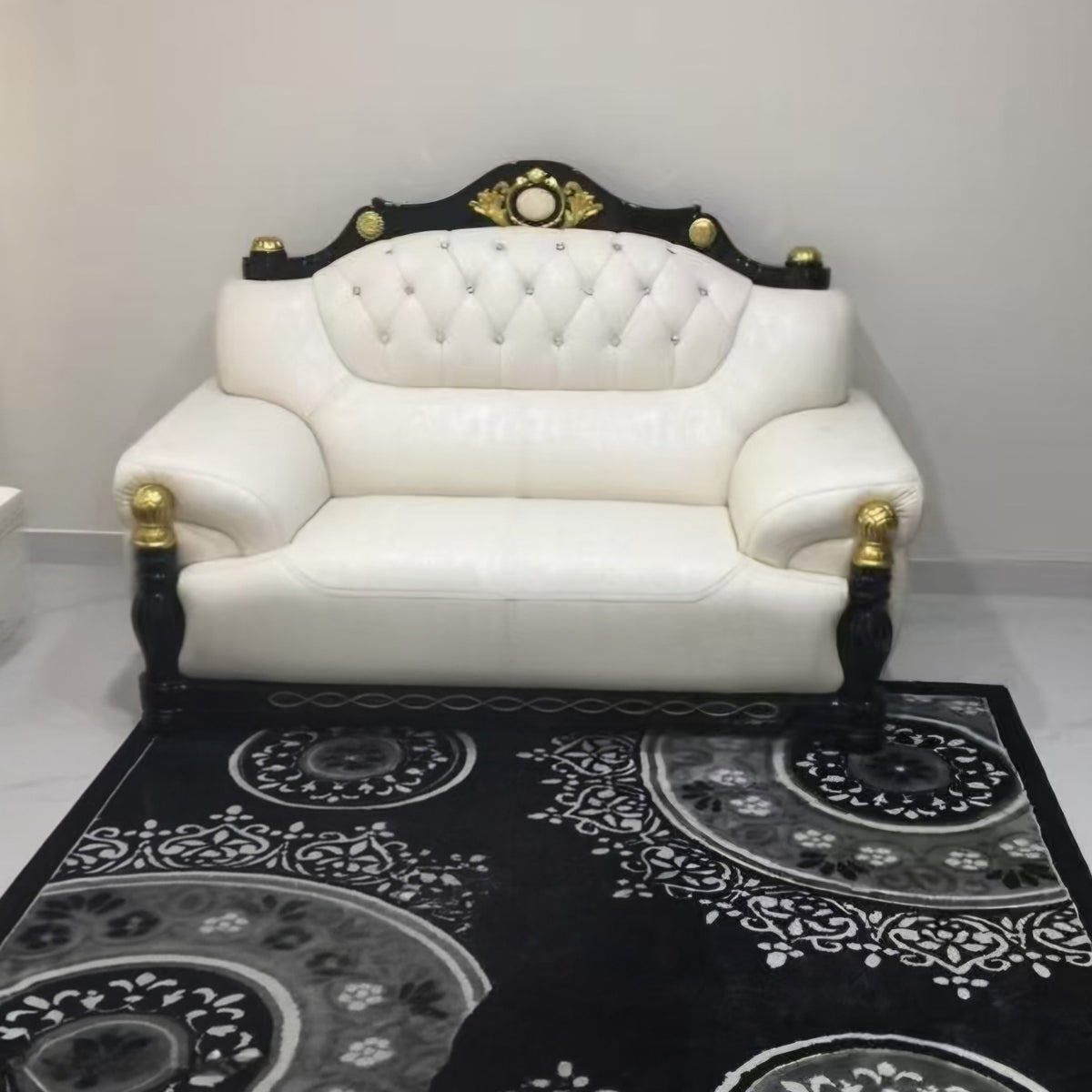 White leather sofa with black and gold accents on a black patterned rug.
