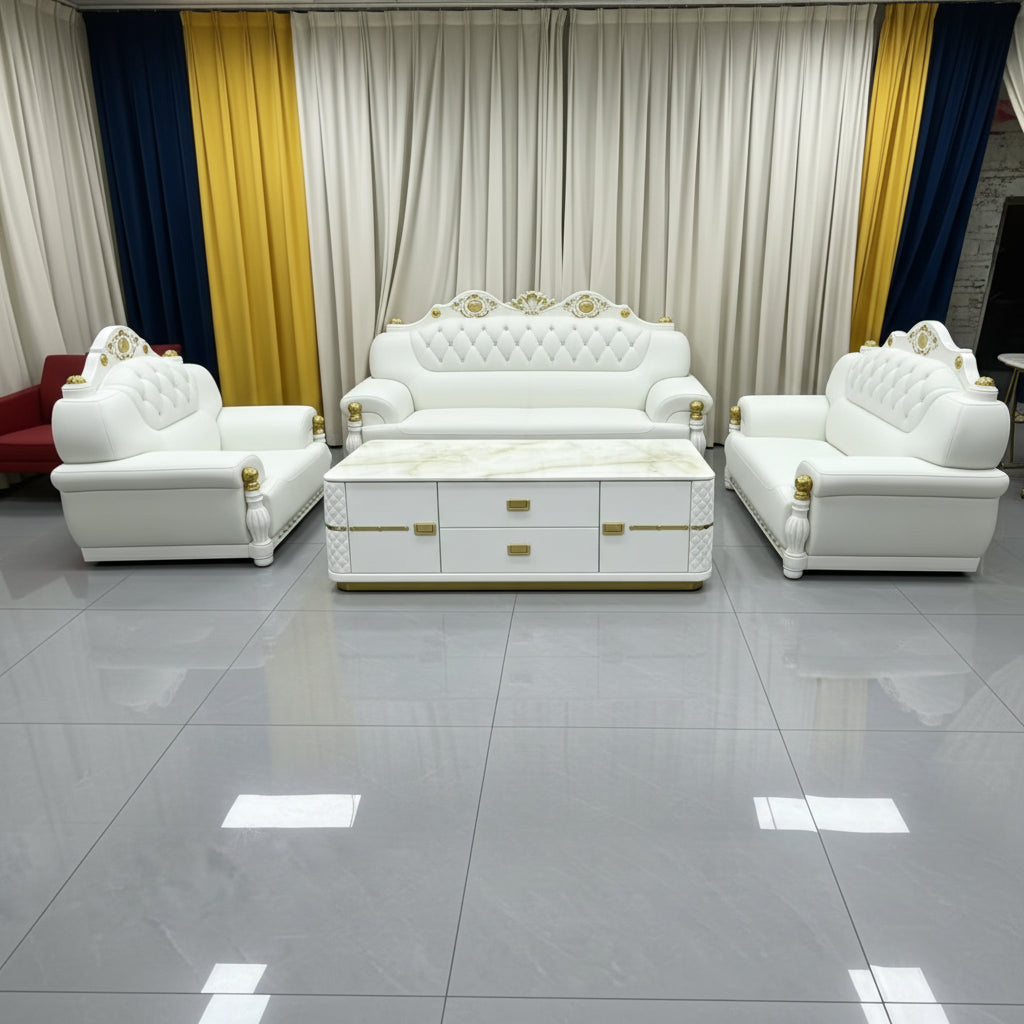 A luxury white leather sofa set with gold accents, including a three-seater sofa, two matching armchairs, and a marble-top coffee table, arranged in a showroom with beige and gold curtains.