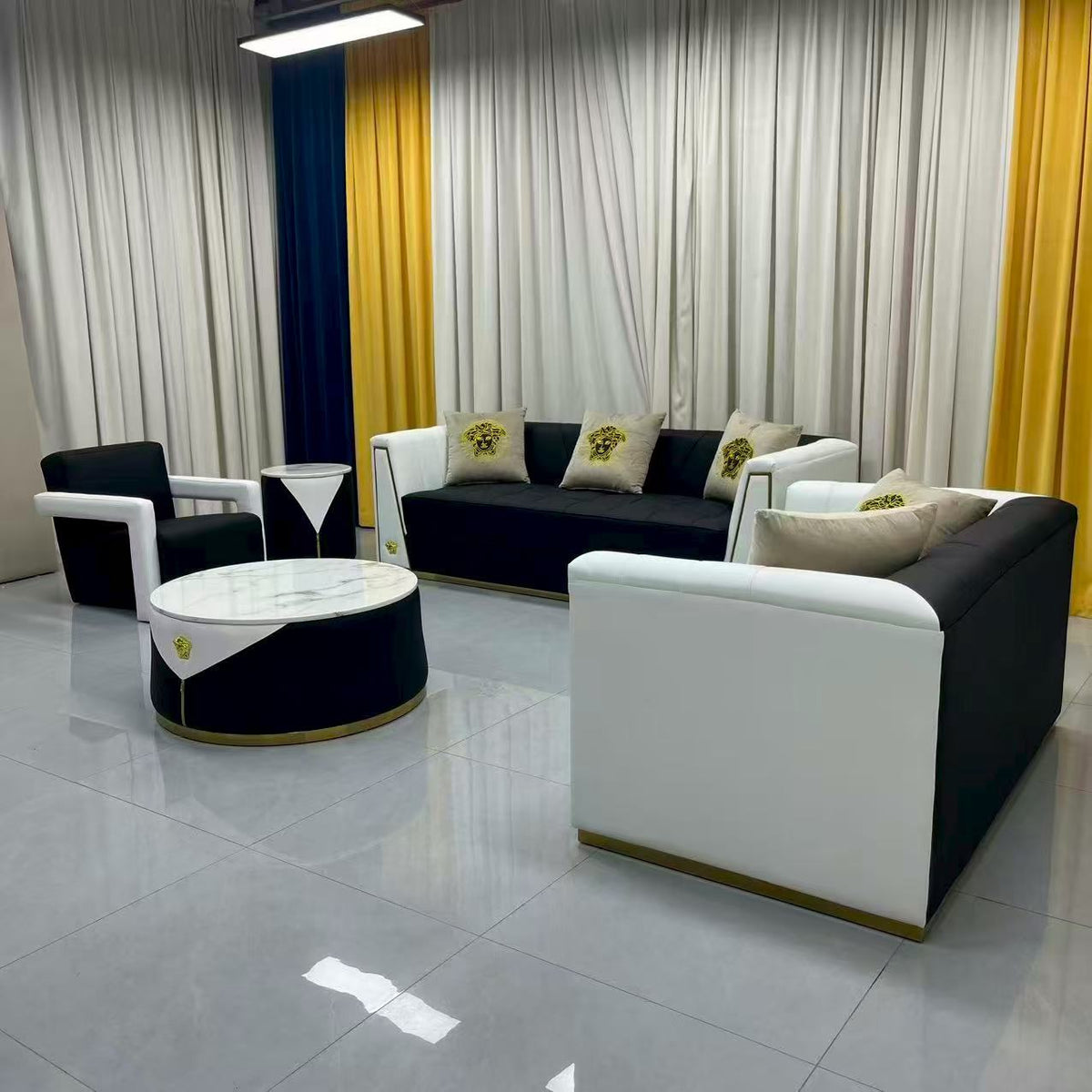 Modern black and white leather sectional sofa set with a matching round coffee table, styled in a showroom with cream curtains, yellow side panels, and a gray tiled floor.